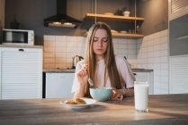 Young female with spoon and bowl enjoying tasty corn rings in kitchen — Stock Photo