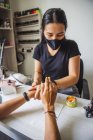 Маникюрша массирует руки безликого клиента после нанесения косметического масла на ногтевую студию — стоковое фото