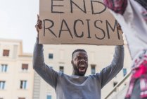 Low angle of African American male activist with End Racism poster screaming on city street during Black Lives Matter protest — Fotografia de Stock
