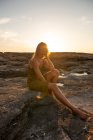 Vue latérale de la jeune femme debout sur le rocher au coucher du soleil et regardant loin — Photo de stock
