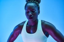 Junge afroamerikanische Sportlerin mit Afro-Zöpfen im Dutt und geschlossenen Augen auf blauem Hintergrund — Stockfoto