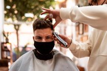 Male hairstylist in eyeglasses making haircut to adult client in hairdressing salon during COVID 19 pandemic — Foto stock