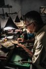 Vue latérale d'un homme ethnique mature travaillant à un bureau endommagé dans un atelier artisanal — Photo de stock