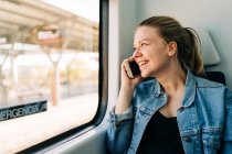 Junge lässige Frau in Jeansjacke telefoniert während des Pendelns aus dem Fenster des Zuges — Stockfoto
