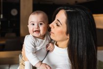 Seitenansicht der entzückten Mutter, die ihr entzückend lächelndes Baby hält, während sie zu Hause zusammen Spaß hat — Stockfoto