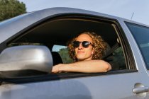 Serious young haired male in stylish sunglasses looking at camera through open window of car while sitting at driver seat — Photo de stock