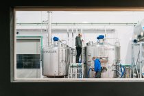 Seitenansicht männlicher Mitarbeiter mit Mundschutz, die während der Coronavirus-Pandemie Schlauch an Metallbehälter in Bierfabrik anschließen — Stockfoto