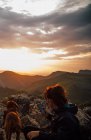 Unrecognizable hiking female using smartphone to take selfie with purebred dog sitting on boulder in high mountains at sundown — Stock Photo
