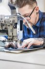 Artesano masculino usando máquina de coser mientras crea tapicería para asiento de moto en taller - foto de stock