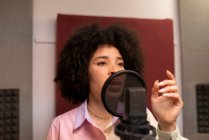 Чорна співачка виконує пісню проти мікрофона з поп-фільтром, стоячи з рукою на стегні і з нетерпінням чекаючи на звукову студію — стокове фото