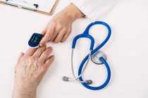 Draufsicht der Ernte unkenntlich Arzt misst Blutsauerstoff des Patienten mit Pulsmesser am Tisch mit Stethoskop in Klinik — Stockfoto