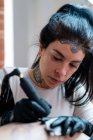 Tatuagem feminina com tatuagem de desenho de máquina no corpo do cliente irreconhecível no salão — Fotografia de Stock
