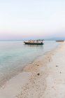 Pequeno barco atracado na calma água do mar azul perto de praia de areia em país exótico no crepúsculo pacífico — Fotografia de Stock