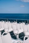 Пустые белые стулья на палубе круизного судна, плывущего в голубой морской воде — стоковое фото