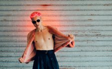 Jovem gay em óculos de sol modernos e casaco de pele elegante com cabelo rosa contra a parede cinza — Fotografia de Stock