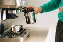 Cortar pessoa irreconhecível com jarro de metal preparando café com máquina profissional à mesa em casa — Fotografia de Stock