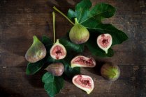 Top view of whole and cut figs with juicy pulp on green foliage with veins on wooden surface — Stock Photo