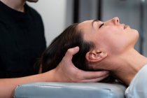 Vue latérale d'un kinésithérapeute masculin massant le cou d'une femme les yeux fermés à l'hôpital — Photo de stock
