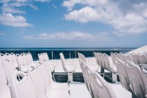 Пустые белые стулья на палубе круизного судна, плывущего в голубой морской воде — стоковое фото