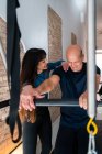 Sorrindo instrutor do sexo feminino ajudando o homem a fazer exercícios sobre pilates reformador durante o treinamento em ginásio — Fotografia de Stock