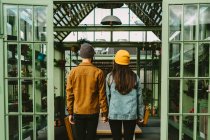 Visão traseira do casal de hipsters na moda em pé no terraço de madeira, segurando as mãos e olhando sobre o ombro — Fotografia de Stock