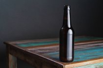 Темная стеклянная бутылка алкогольного напитка на окрашенном деревянном столе квадратной формы дома — стоковое фото