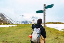 Back view of female backpacker pointing on arrow showing footpath direction standing against pole in Peak of Europe — Stock Photo