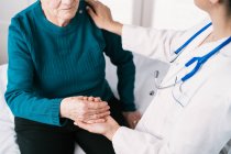 Crop médico anônimo falando com a mulher idosa enquanto segurando as mãos durante o exame no hospital — Fotografia de Stock
