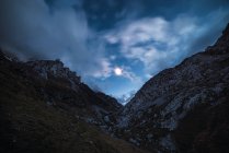 Низький кут скелястого гірського хребта під темним небом з туманними хмарами в м'якому світлі — стокове фото
