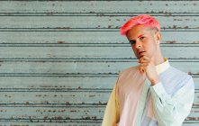 Auto confiante pensativo jovem gay no moderno vestuário com rosa cabelo e tatuagens olhando para câmera — Fotografia de Stock