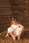 Alegre adorable niño en overoles jugando con heno sentado en fardos de paja en el campo - foto de stock