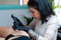 Tatoueuse avec tatouage de dessin de machine sur le corps d'un client méconnaissable dans le salon — Photo de stock