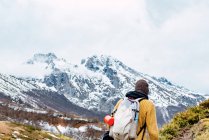 Vista posterior de turista anónimo con mochila de pie sobre césped cubierto de nieve en el valle de las montañas en los picos de Europa - foto de stock
