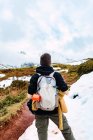 Вид сзади анонимного туриста с рюкзаком, стоящим на снежной лужайке в долине гор на вершинах Европы — стоковое фото