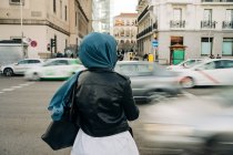 Back view of anonymous Muslim female in hijab standing near road with busy traffic in rush hour — Foto stock