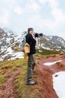 Vista lateral turista feminino de corpo inteiro com mochila usando câmera fotográfica enquanto fotografa a incrível natureza dos picos da Europa durante a viagem — Fotografia de Stock