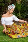 Веселая молодая этническая женщина в декоративной африканской юбке против пальмовых растений на лугу — стоковое фото