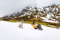 Glückliche Frau rutscht mit Schnee bedeckten Hang hinunter, während glücklicher Englischer Setterhund in den Bergen beiseite läuft — Stockfoto