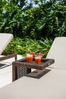 Glasses of fresh yummy watermelon squeezed juice served on small wicker rattan table near comfortable sunbed in tropical resort on sunny summer day — Stock Photo