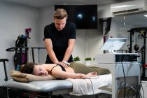 Männlicher Physiotherapeut, der während der medizinischen Behandlung im Krankenhaus Laser auf die Rückenhaut der Frau aufträgt — Stockfoto