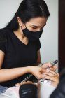 Female master using electric nail file while doing manicure for client in beauty salon — Stock Photo