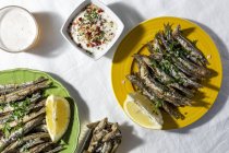 From above of traditional Spanish fried boquerones served on plates with lemons and bowl of white soup placed on table with glass of beer in restaurant — Photo de stock