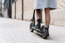 Cropped unrecognizable female in casual wear riding scooter on paved sidewalk — Photo de stock