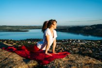 Side view of happy young female traveler in activewear smiling while practicing Upward Facing Dog with Neck Stretch yoga asana on rocky cliff under cloudless blue sky — Stock Photo