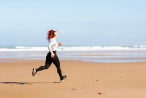 Vista laterale del jogger femminile attivo che corre sulla riva dell'oceano durante l'allenamento in estate — Foto stock
