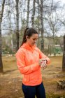 Female athlete in sportswear watching heartbeat on wearable bracelet during break from training in park on blurred background — Fotografia de Stock