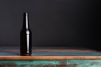 Botella de vidrio oscuro de bebida alcohólica en mesa de madera cuadrada pintada en casa - foto de stock
