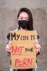Mujer étnica en máscara protectora de pie con mi vida no es su póster de cartón porno durante proteger contra el acoso sexual y la agresión - foto de stock
