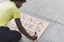 High angle side view of cropped African American female activist writing Black Lives Matter and making placard for protest against racism in city — Stock Photo