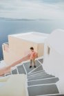 Сверху безликий молодой мужчина в стильном сарае, стоящем на старой каменной лестнице в аутентичной прибрежной деревне с белыми домами и восхищающимся бурлящим голубым морем в Греции — стоковое фото